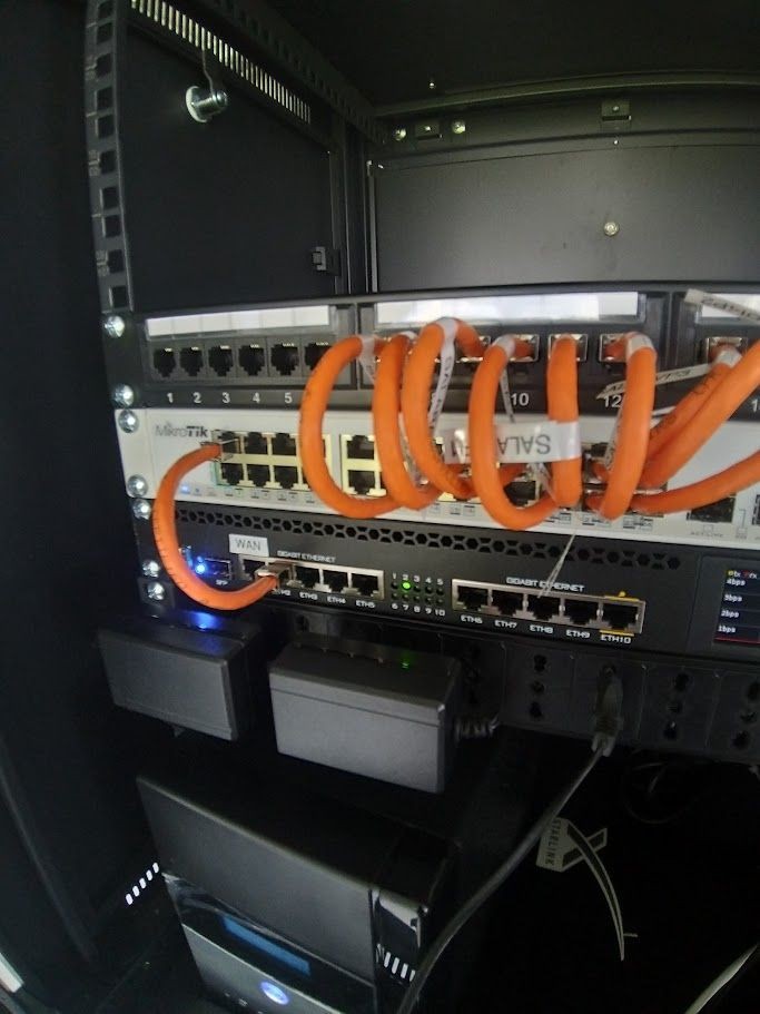 Network server rack with orange cables connected to routers and switches, LED lights on.